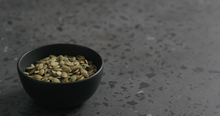 pumpkin seeds in black bowl on terrazzo countertop with copy space