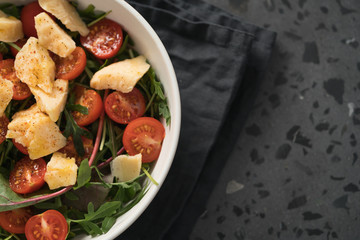 salad with cherry tomatoes, mixed grens and cheese in white bowl on concrete background