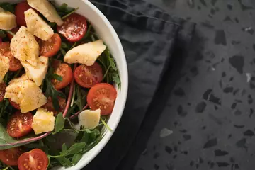 Fototapeten salad with cherry tomatoes, mixed grens and cheese in white bowl on concrete background © GCapture