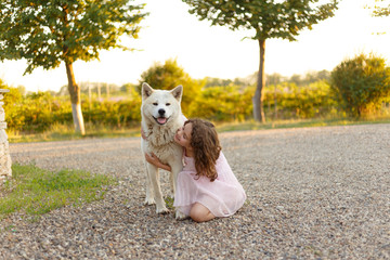 Full length portrait of an adorable little girl hugs her big dog spending time together outside in the summer.