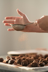 young female hands sprinkle fresh chocolate truffles with cocoa powder on concrete countertop