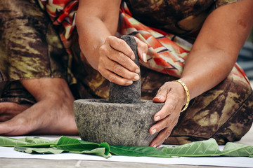 Closeup shot of hands of an Indian female grinding leaves to make paste using Mortar and Pestle. - obrazy, fototapety, plakaty