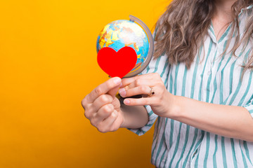 Close up photo of woman hands holding paper heart and globe.