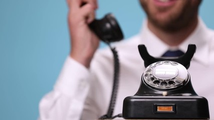 close up on a retro telephone answered by an businessman talking, laughing, hanging up and pointing at camera on blue background