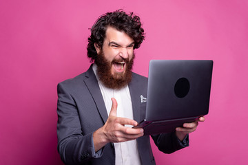 Photo of shocked bearded man in casual looking at laptop.
