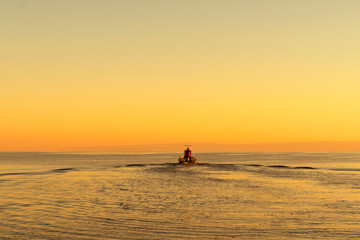 Obraz premium Fisherman on boat at the sunset. Beautiful sunset with the fishing boat. Fishing motor boat with angler. Ocean sea water wave reflections at the sunset. Motor boat in the ocean.