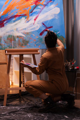 Back view of artist in art studio working on impressionism painting. Modern artwork paint on...
