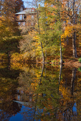 Trees in autumn colors reflecting in the water surface of the lake with a house on the hill