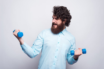 Photo of bearded man in casual wearing blue shirt working with small dumbbells.