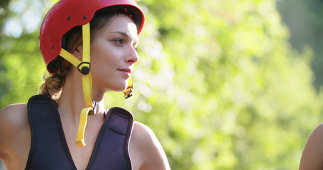 woman wearing life jacket and sport helmet smiling before rafting river descent.Group of people...