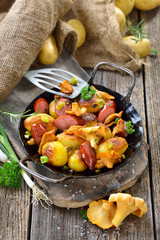 Deftige Kartoffelpfanne mit frischen Pfifferlingen und Cabanossi rustikal in der Eisenpfanne serviert – Hearty fried potatoes with fresh chanterelles and kabanos sausage served in an iron pan