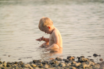 A little boy sits waist-deep in water and throws rocks