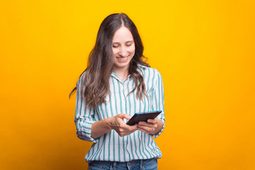 Photo of young woman in casual using tablet over yellow background.