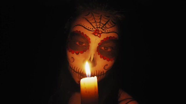 Portrait of a girl with Сatrina Calavera makeup. The girl looks at a burning candle