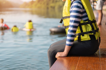 Asian woman wear life jacket sit near river, selective focus, with copy space.