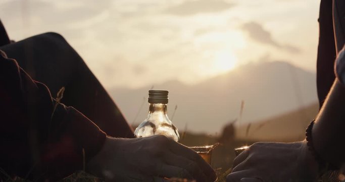 Friends toast or salute with liquor or liqueur of mountain pine Pinus mungo enjoy sunset golden sun light hiking in autumn or fall hike unrecognizable hand glass close up slowmotion flare