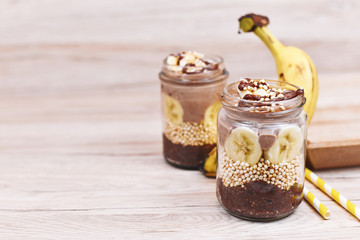 Healthy layered dessert with banana fruit slices, puffed quinoa grain and chocolate chia seed pudding in jar with copy space