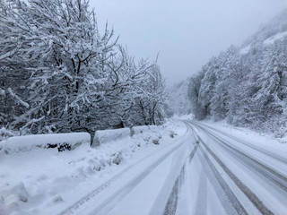 Obraz premium The road along a snow-covered serpentine road in the mountains during a blizzard. Even with a minimum speed, such a trip is very dangerous at any moment an avalanche can break out