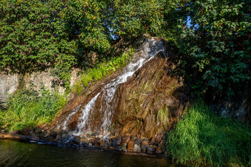 Detail of a small waterfall flowing down a rock into a pond.