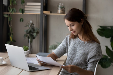 Pensive young Caucasian woman sit at desk at home reading paper letter correspondence thinking pondering, thoughtful millennial female distracted from computer work consider postal paperwork document