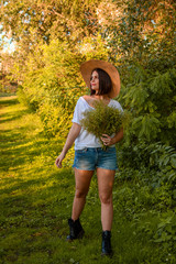 Beautiful young brunette enjoying sunset. Girl is wearing straw heat, white shirt and blue shorts....