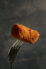 Homemade traditional spanish croquettes on a fork with dark background. Tapas food.
