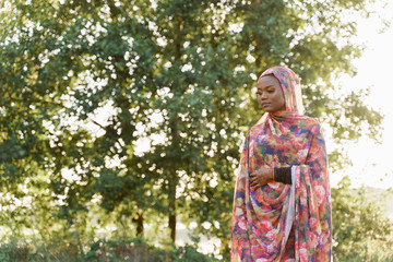 Attractive muslim black girl weared in hijab smiles and looks left side. African woman in national colorful dress on green background. Life style of black girl wearing in scarf named hijab
