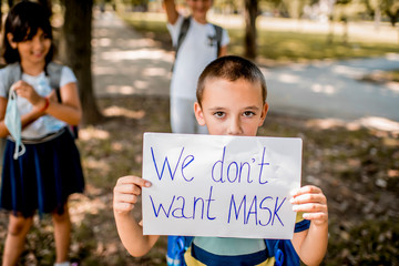 School child holding a paper with text " We don t want mask"