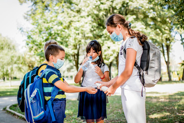 Girl sanitizing school child hands outdoors