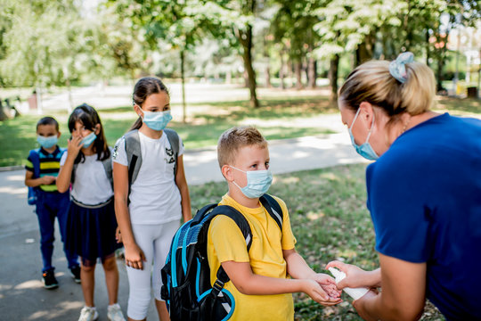 Woman Sanitizing School Children's Hands Outdoors