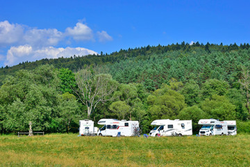  Camper vans  parked on a grassy campground in summer sunny day. Campsite in the middle of nature.