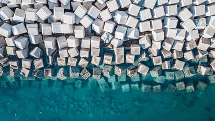Aerial view of a young man on a cement cube blocks protecting the shore from the waves in the port of Malaga, Spain.