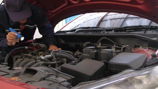 Asian Man mechanic inspection Shine a torch car engine checking bug in engine from application smartphone.Red car for service maintenance insurance with car engine.for transport automobile automotive