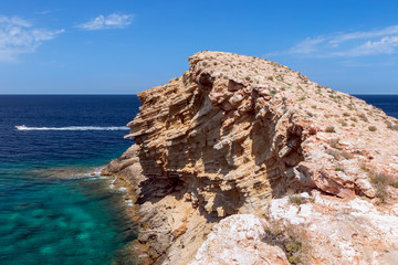 A wave frozen in stone in the emerald sea with speed boat. Cape Punta Galera. Ibiza, Balearic Islands, Spain.