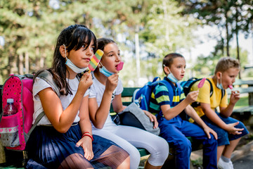 Group of children eating ice cream  outside. They are wearing a protective face mask down.