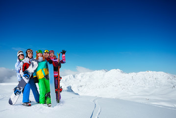 Group of young adults snowboarders stand on top of the mountain together over snow covered peaks on...