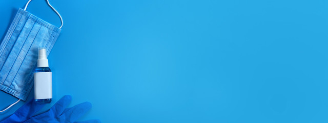 Top view surgery mask with blue spray alcohol bottle (Ethanol or ethyl alcohol) and latex gloves for medical purpose prevent from coronavirus COVID-19 on plain blue isolated background with copy space