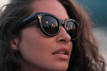 Fototapeta premium Close-up of young beautiful woman with curly hair in sunglasses standing outdoors