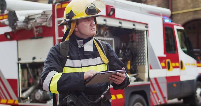 Portrait of fireman in helmet and gull equipment viewing on sides and writting data to tablet. Rescuer working with latest technologies. The concept of saving lives, heroic profession, fire safety
