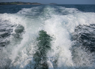 Wake from a motorboat sailing along the menai strait at anglesey. Puffin island and the coast with blue sea and a summer sky.