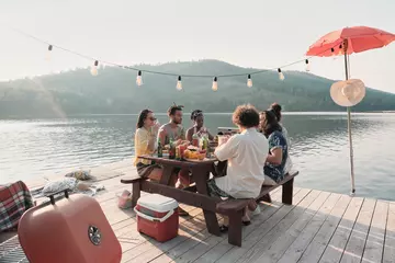 Fototapeten Group of friends sitting at the table and have dinner on a pier with beautiful landscape of the lake © AnnaStills