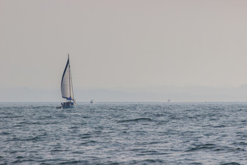 Obraz premium Sailing boat with a white sail on the ocean in summer. Blue sky and blue sea