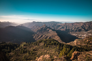 A panorama view of a sunset over the Roque Nublo in Gran Canaria, Spain. Tenerife is visible in the background.