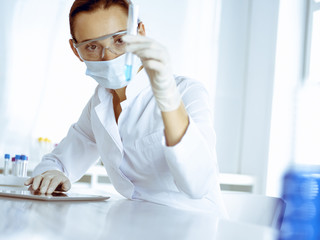 Female laboratory assistant analyzing test tube with blue liquid. Medicine, health care and researching concept