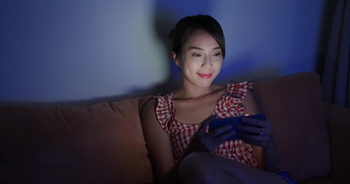 Woman watch on cellphone and sit on sofa at home in the evening