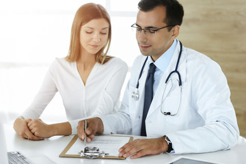 Doctor and patient discussing medical exam results while sitting at the desk in sunny clinic