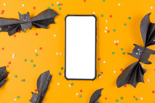 Smartphone is surrounded by bats made of paper. Orange background with decorative stars. Mock up. The concept of Halloween and technologies