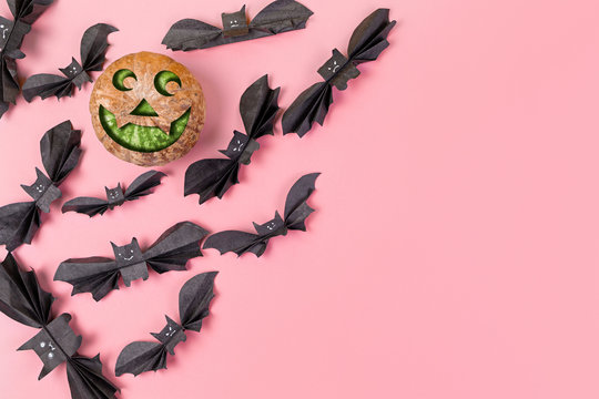 A pumpkin with a face surrounded by bats made of paper. Purple background. Copy space. Flat lay. The concept of Halloween, and holiday decorations