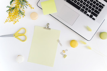 Top view of office desk workspace with laptop, clipboard mock up, stationery, colorful macaroons...