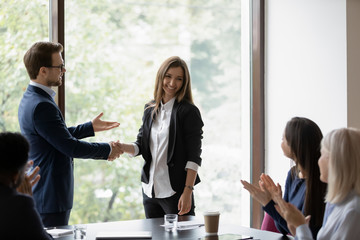 Male businessman ceo executive shaking hand of smiling happy millennial woman manager hiring her on meeting, company workers clapping hands welcoming new female teammate presented by boss employer